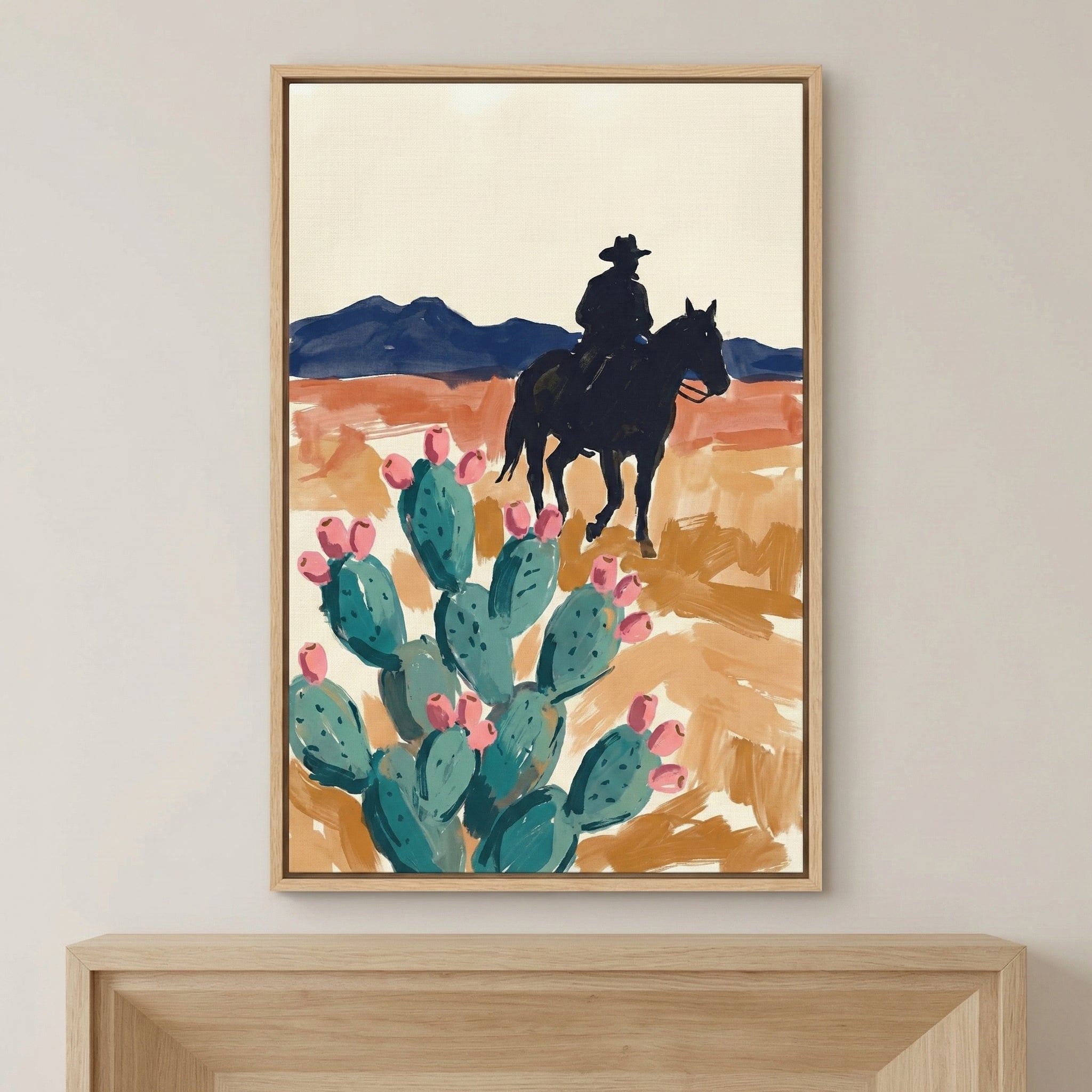 Framed painting of a cowboy on horseback riding through a desert landscape, with a blooming prickly pear cactus in the foreground. The artwork uses bold brushstrokes and earthy tones to evoke a classic western scene.