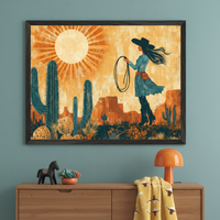 Modern room with a wooden dresser. A large framed desert art print hangs centered above, depicting a woman in a cowboy hat with a lasso, saguaro cacti, and a bright sun in an illustrative style. On the dresser are a horse figurine, succulent, and orange lamp.