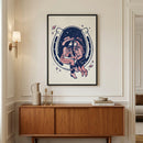 Framed artwork featuring two cowgirls sitting close together inside a large horseshoe, set against a cosmic background with stars and planets, hangs above a mid-century modern wooden console. The room has elegant wall molding, warm lighting, and minimalist decor with ceramic vases and stacked books.
