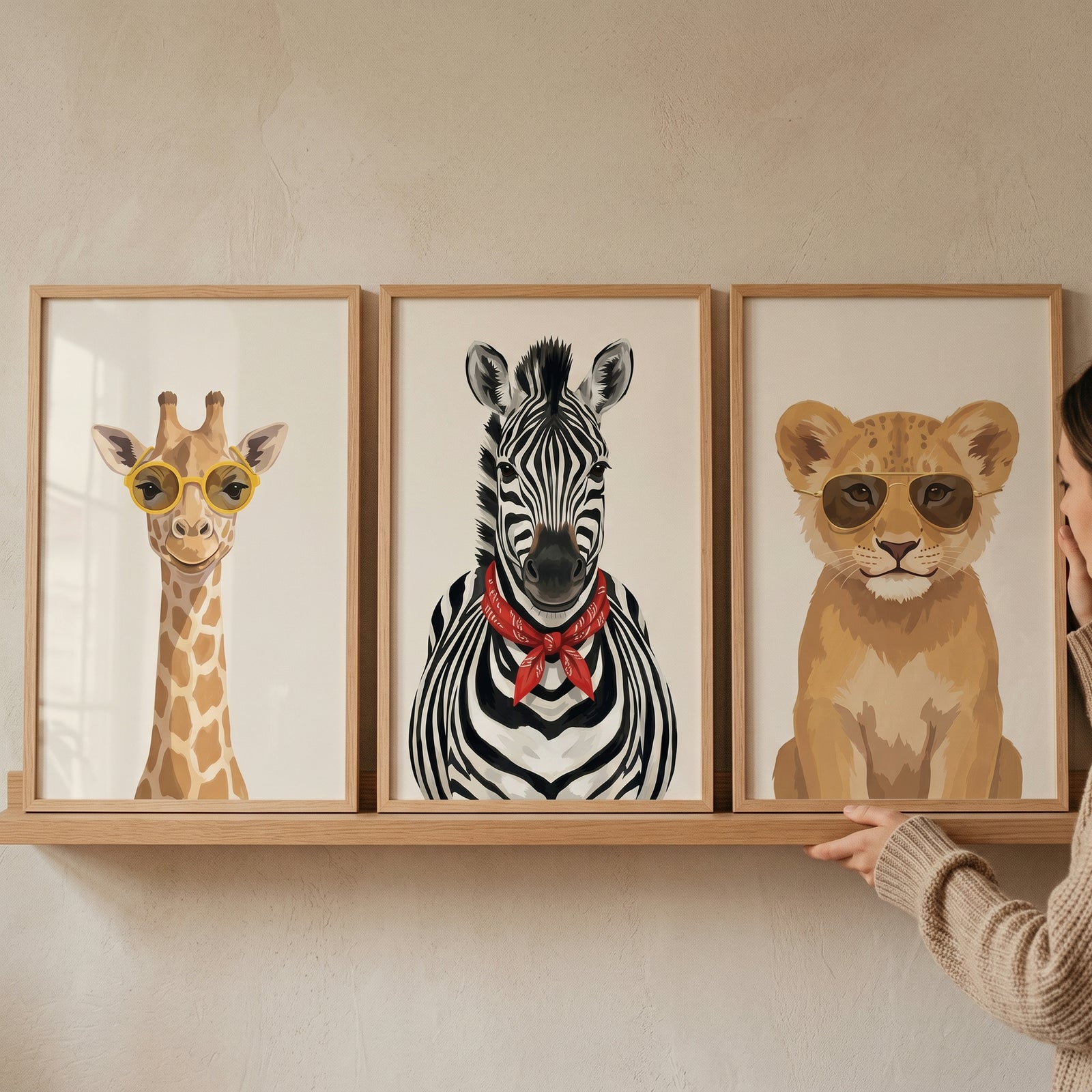 Cream safari animal wall art set of 3 with a giraffe, zebra, and lion cub wearing glasses and a scarf on a shelf.