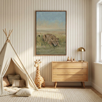 A serene and warm nursery with vertical striped cream wallpaper. In the center of the wall hangs a large framed canvas artwork depicting a lioness stalking through tall grass under a soft blue and beige sky. To the left, there is a cream fabric teepee filled with cozy pillows and a tall, realistic plush giraffe toy standing beside it. To the right, a three-drawer light wood dresser holds a modern brass dome-shaped lamp and simple wooden toys. 