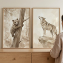 Two vertical wooden frames with watercolor-style art sit atop a light-toned wooden dresser. The left frame features an illustration of a brown bear cub climbing a tree and looking forward. The right frame shows a wolf standing on a rocky outcrop, its head tilted upward toward the sky. Both pieces are rendered in soft, neutral shades of beige and brown. A person in a light-colored sweater is partially visible on the right side as they look at the two pieces of art.