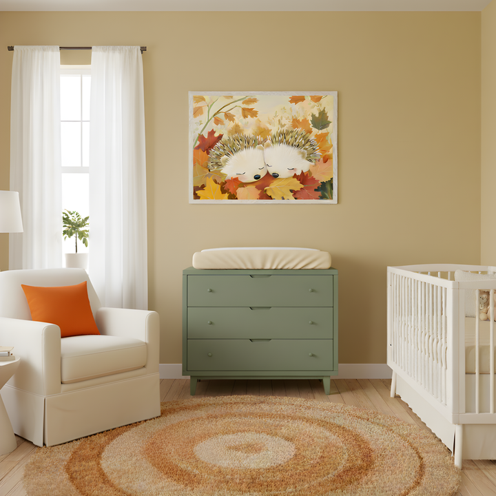 Bright nursery decorated in warm autumn tones, featuring a framed illustration of two sleeping hedgehogs nestled in colorful fall leaves above a sage green changing table. The room includes a white crib, a soft cream glider with an orange accent pillow, and a circular rug in earthy shades of rust and beige.