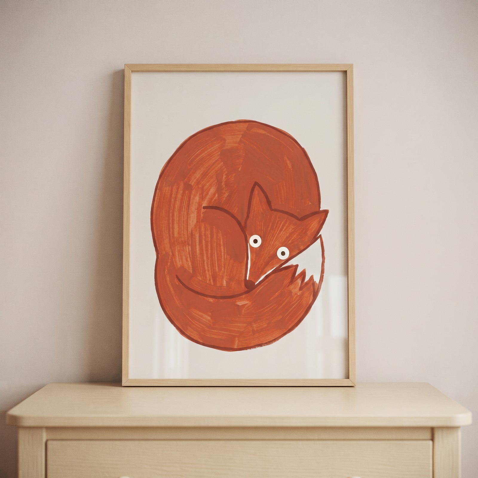 Minimalist curled up red fox wall art in a light wood frame displayed on a dresser against a neutral wall.