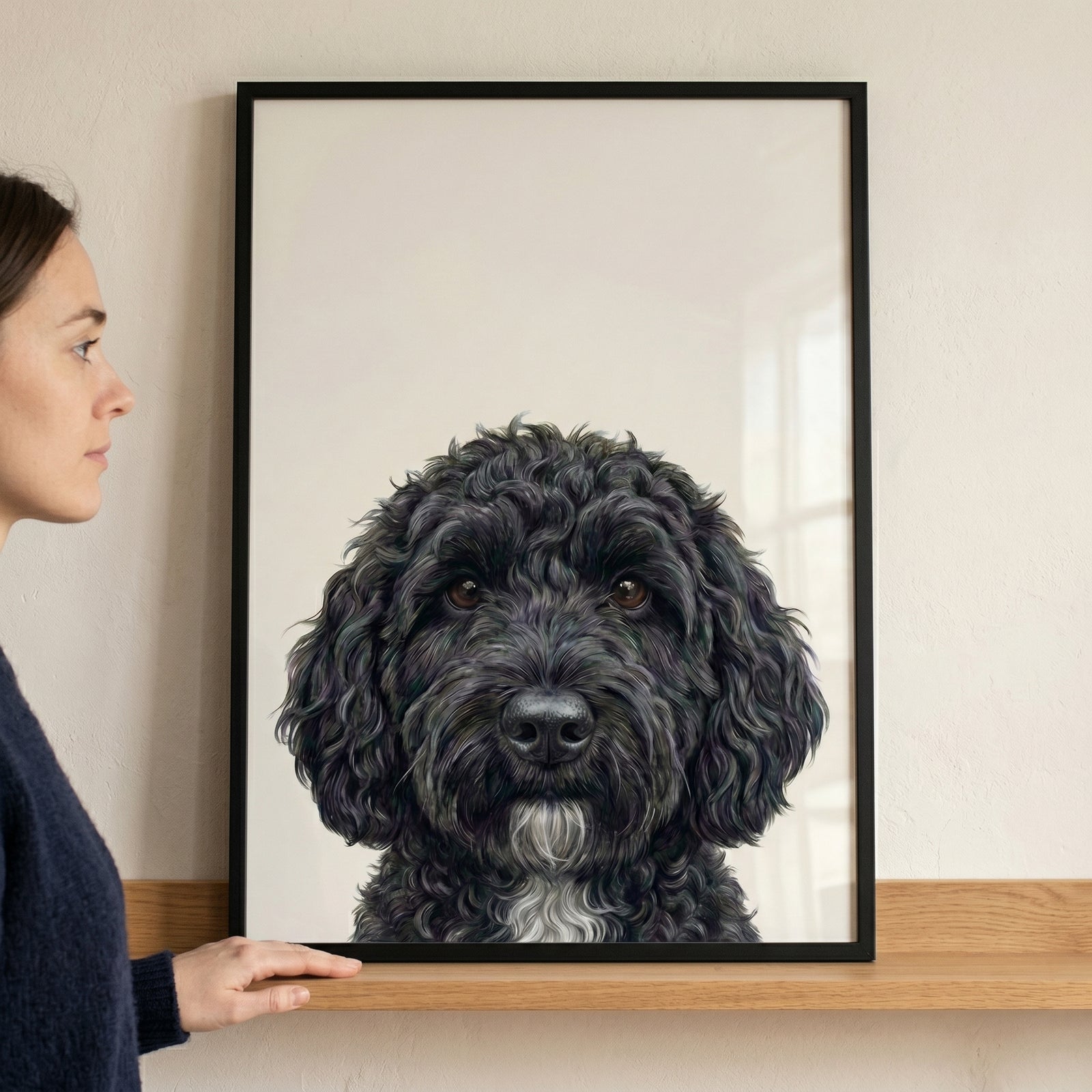 Curly black doodle dog wall art in a black frame held on a shelf. The dog has dark eyes and a white chest patch.