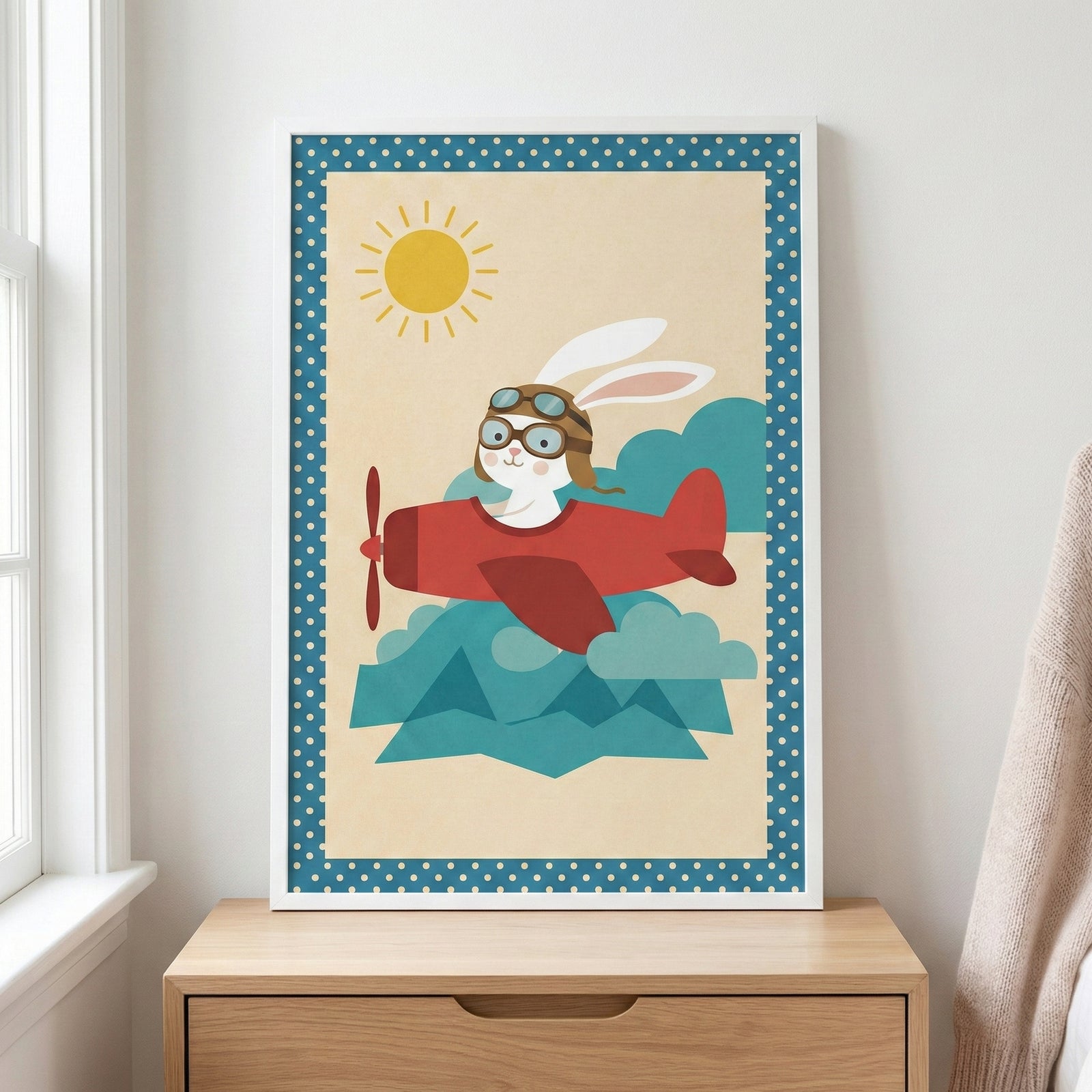 A framed nursery-style illustration of a white rabbit wearing an aviator helmet and goggles while flying a red propeller airplane. The scene is set against a pale background with a bright yellow sun and stylized blue clouds, bordered by a blue frame with white polka dots. The framed art sits on a light-colored wooden dresser next to a window with white trim.