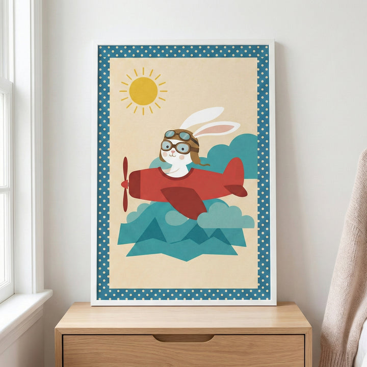 A framed nursery-style illustration of a white rabbit wearing an aviator helmet and goggles while flying a red propeller airplane. The scene is set against a pale background with a bright yellow sun and stylized blue clouds, bordered by a blue frame with white polka dots. The framed art sits on a light-colored wooden dresser next to a window with white trim.