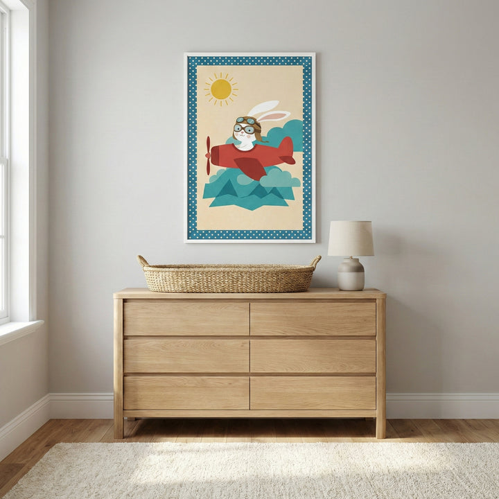 A nursery or child's bedroom featuring a light wood six-drawer dresser against a soft grey wall. On top of the dresser is a long, oval wicker basket and a small, modern table lamp. Centered above the dresser is a white-framed piece of art showing a white rabbit in an aviator hat flying a red propeller plane over green mountains. The artwork is bordered by a blue and white polka dot pattern. A neutral-toned rug is on the floor, and natural light comes from a window on the left.