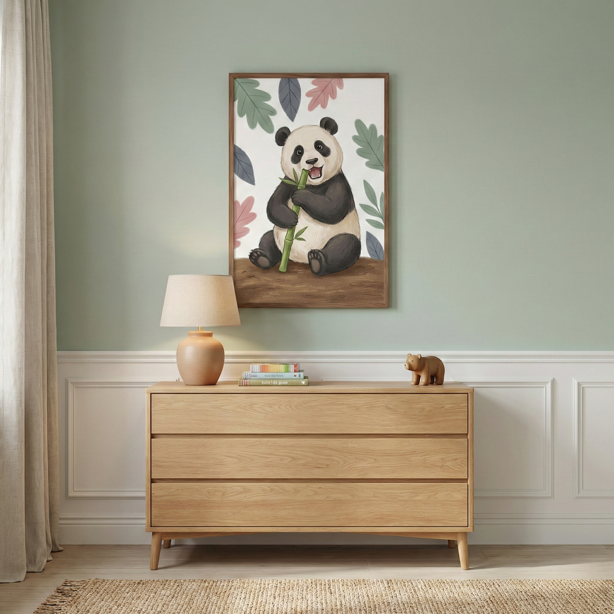 A child’s bedroom scene features a framed illustration on a sage green wall above a light wood three-drawer dresser. The artwork depicts a cute cartoon giant panda sitting and eating a stalk of green bamboo, surrounded by colorful leaves. On top of the dresser sits a small terracotta-colored lamp with a neutral shade, a stack of books, and a small wooden bear figurine. The wall has white wood paneling on the bottom half, and a woven jute rug is on the floor. A white curtain is at the left.