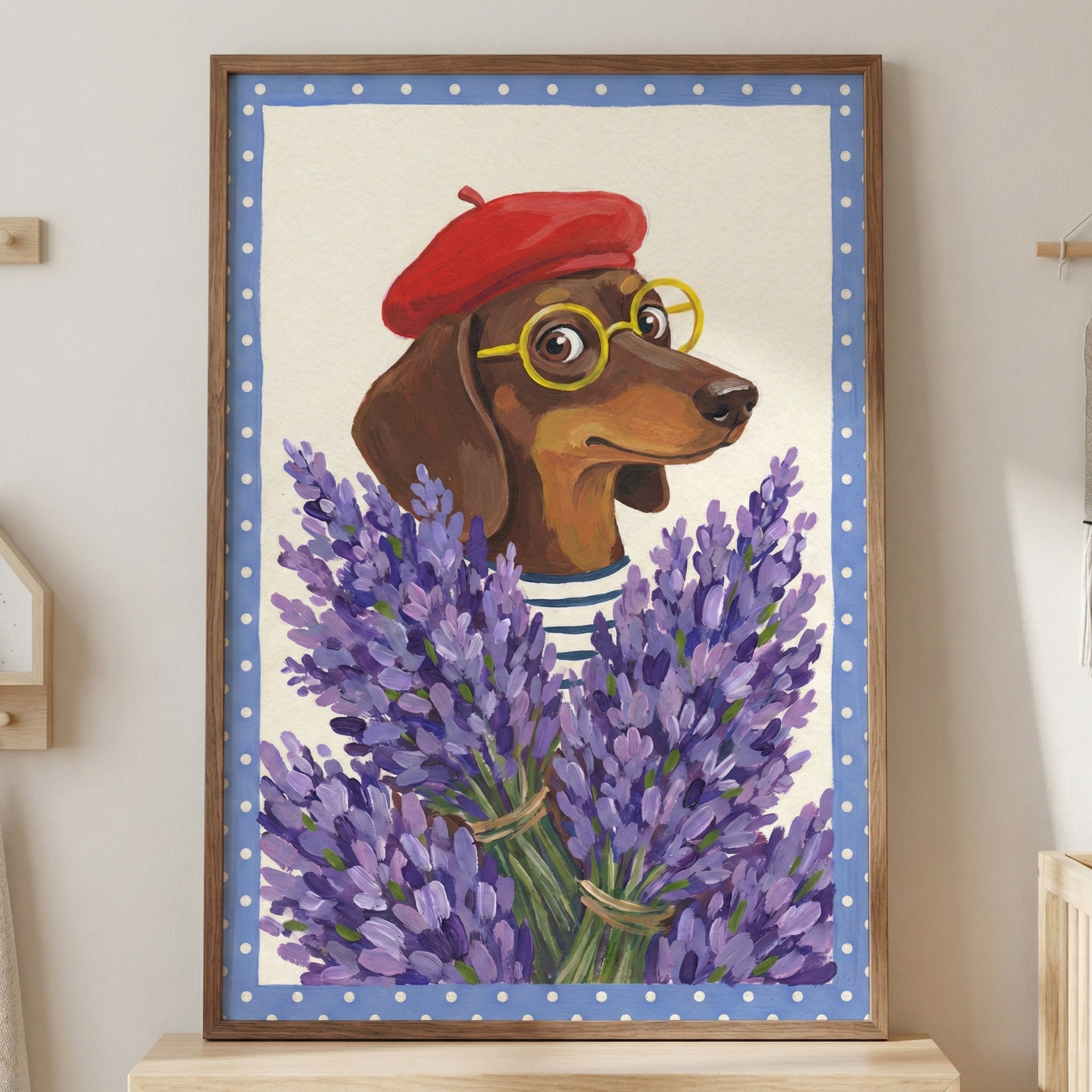 A vertical framed artwork depicting a brown dachshund dog wearing a red beret, yellow round-framed glasses, and a blue-and-white striped shirt. The dog is positioned behind a large, dense bouquet of purple lavender. The illustration has a cream background and a light blue border with white polka dots, all set within a wooden frame leaning against a wall.