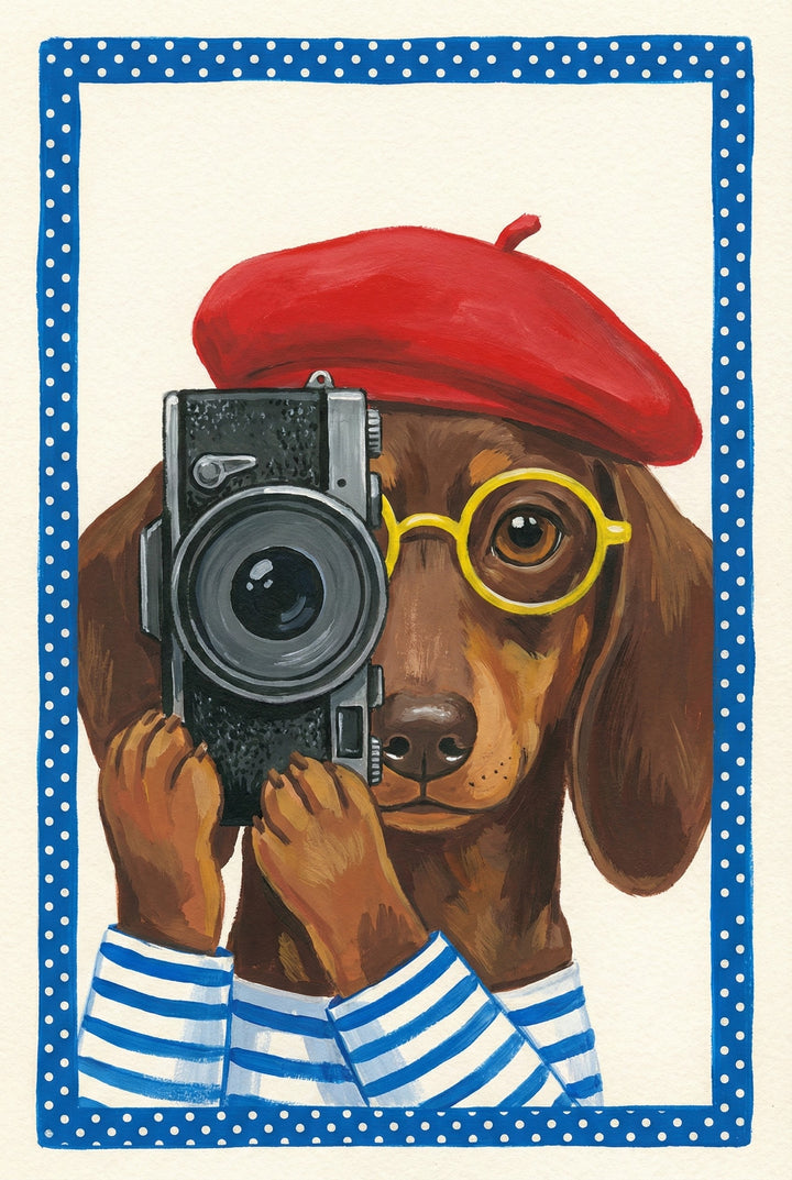 Dachshund wearing a red beret and glasses holding a vintage camera up to its eye, as if taking a photo, with a dotted blue frame.