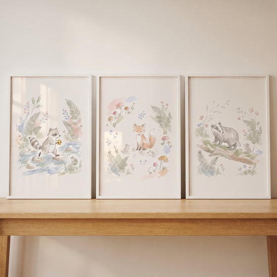 Watercolor raccoon, fox, and badger art. Dainty fern woodland animals wall art set of 3 on a light wooden table.