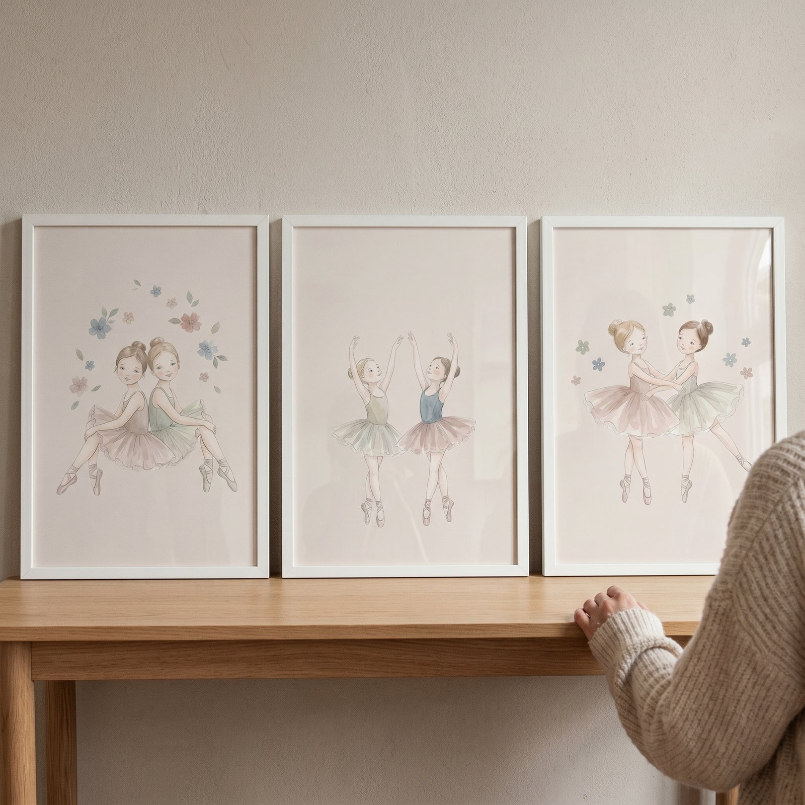 A dainty neutral little ballerina wall art set of 3 in white frames sits on a wooden table against a light wall.