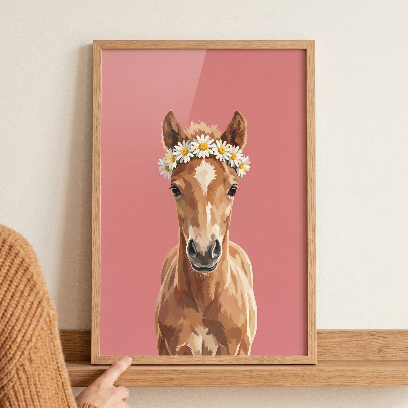 Daisy crown brown foal wall art in a wooden frame set against a pink backdrop on a shelf.