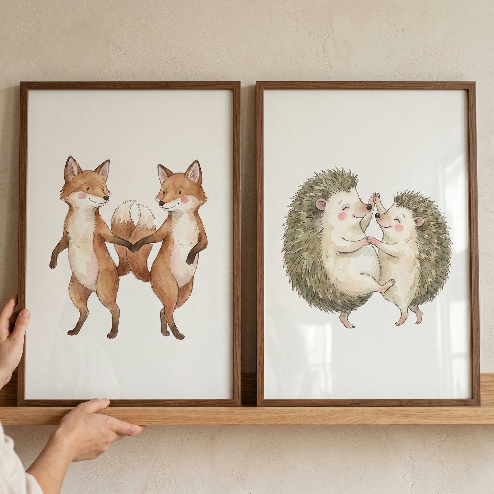 Dancing woodland animal wall art set of 2 featuring watercolor foxes and hedgehogs in frames on a wooden shelf.