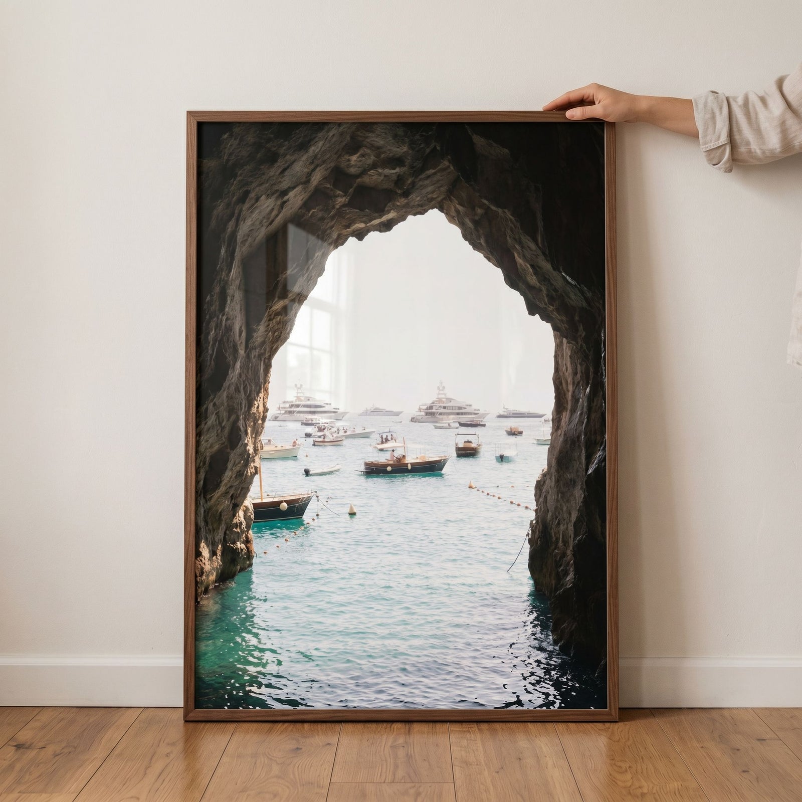 Dark coastal sea cave wall art in a wood frame showing yachts on the ocean from inside a rocky cavern.