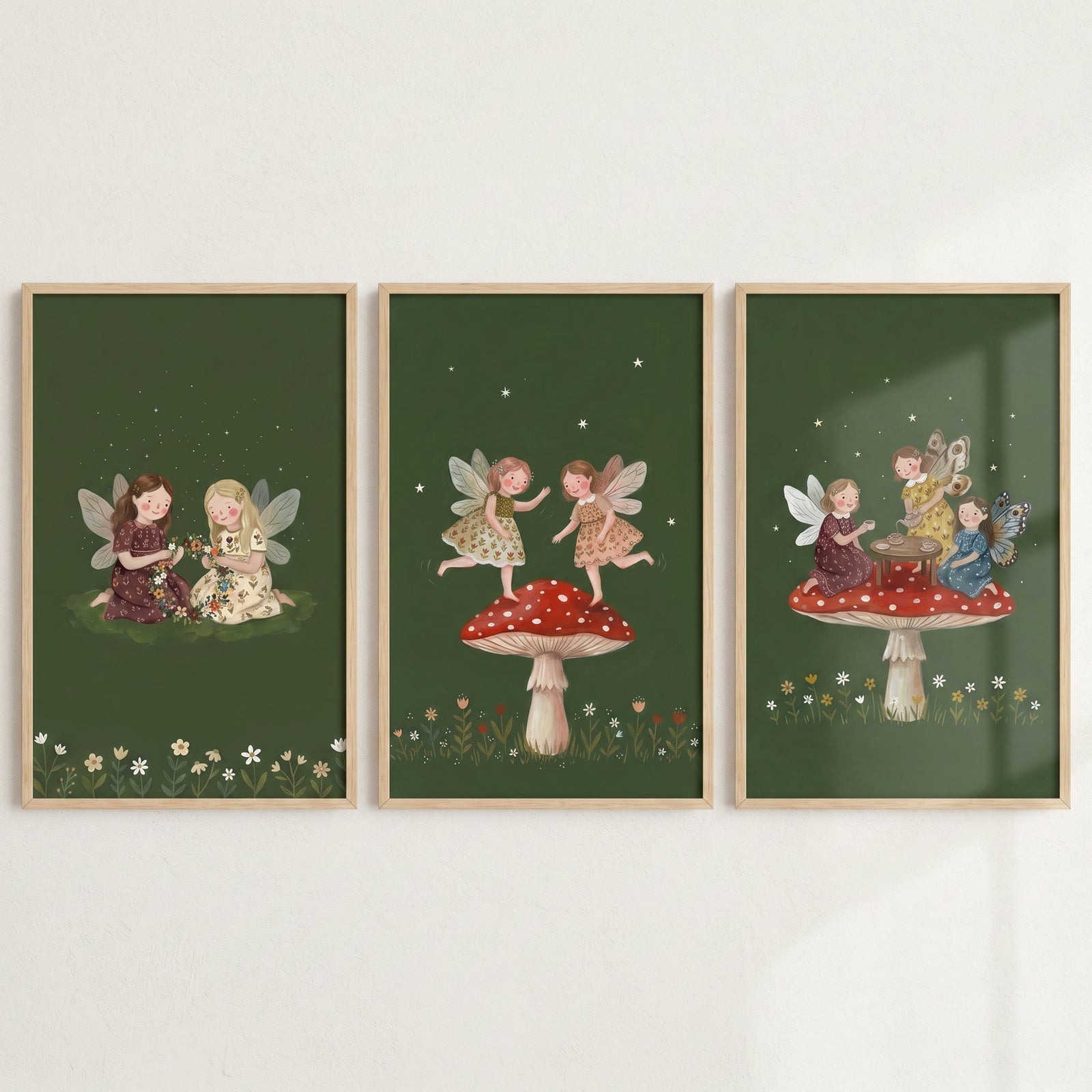 Dark olive forest fairies wall art set of 3 depicts winged figures sitting on grass and atop red spotted mushrooms.