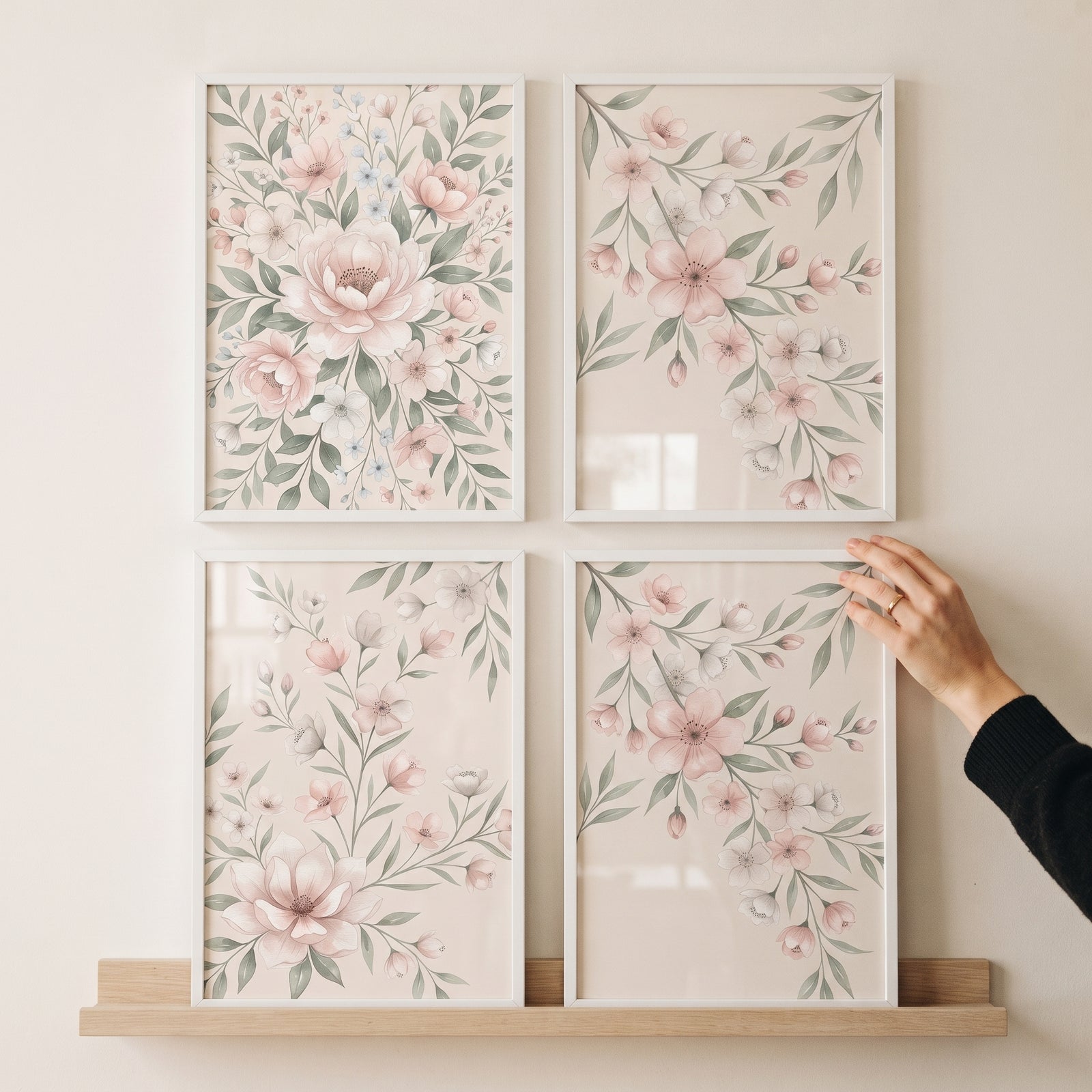 Hand touches delicate blush garden wall art set of 4 botanical prints in white frames above a wooden shelf.