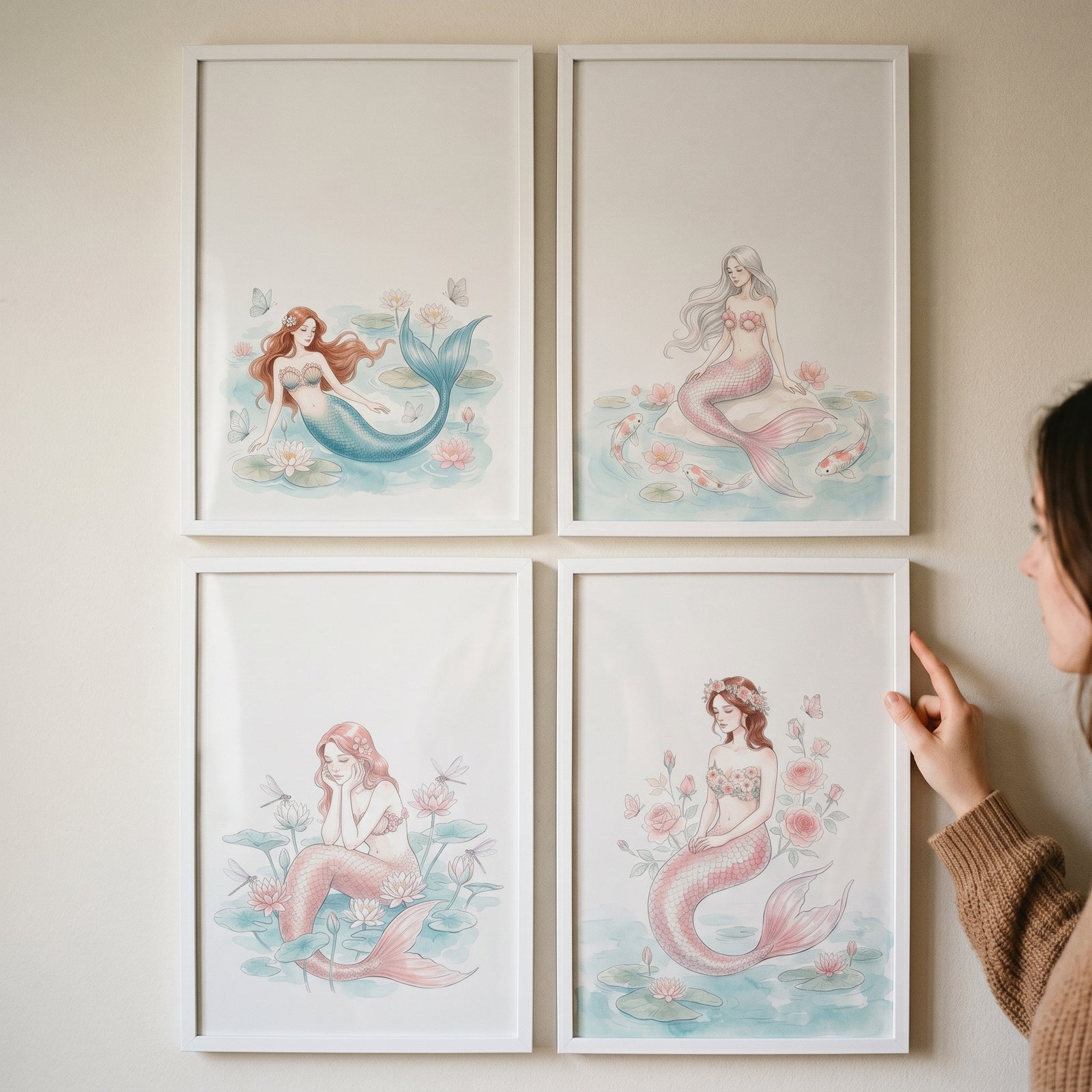 Hand adjusts a delicate fairytale watercolor mermaid wall art set of 4 framed prints on a neutral wall.