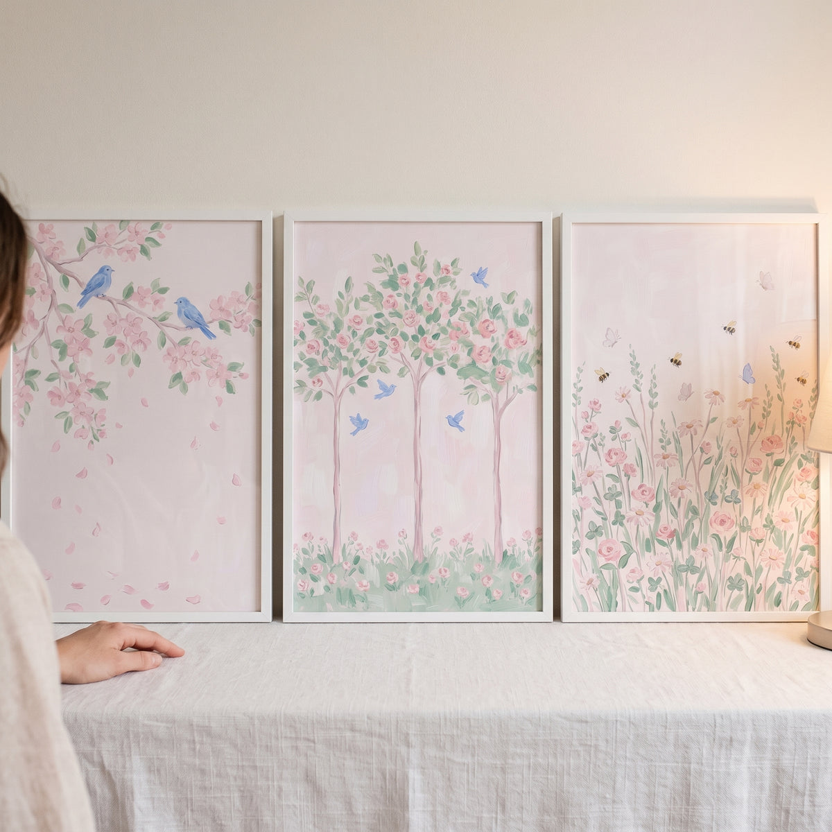 Delicate spring pink garden wall art set of 3 depicts birds, blossoms, and trees in white frames on a white tablecloth.