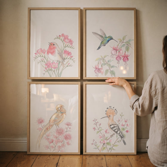 A person touches a delicate watercolor botanical birds wall art set of 4 featuring various birds and pink blossoms.