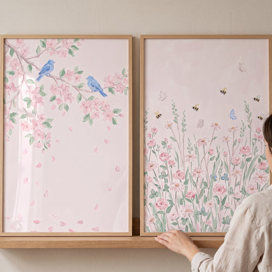 Delicate watercolor pink garden wall art set of 2 with blue birds on cherry blossoms and a wildflower field on a shelf.