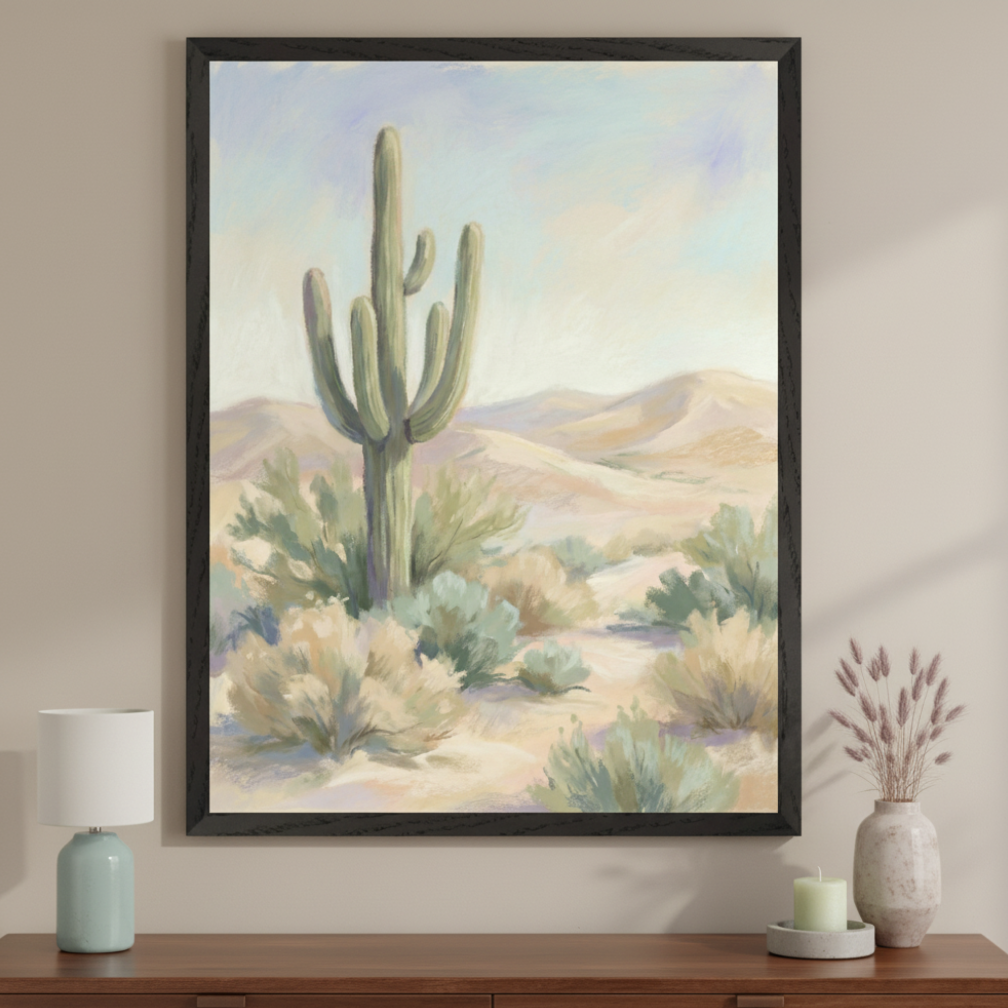 Contemporary room with a dark wood dresser. A large, black-framed desert landscape painting with a saguaro cactus, shrubs, and dunes under a pale sky hangs centered above the dresser. A light blue lamp and dried floral vase are on the dresser.