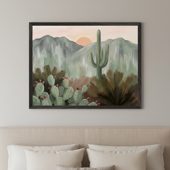 Neutral bedroom with a beige upholstered headboard and pillows. A framed painting of a desert landscape hangs above the bed. It depicts saguaro and prickly pear cacti, mountains, and a sunset in a painterly style.