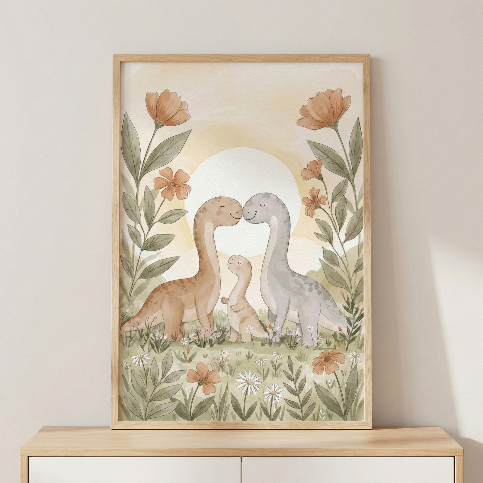 A vertically framed watercolor-style illustration features three long-necked dinosaurs in soft, pastel tones. A larger earthy brown dinosaur and a grey one lean their heads toward each other over a smaller brown dinosaur, creating a sweet family scene. They stand in a field of grass and wildflowers under a large, pale sun. Tall, stylized orange floral stalks frame the scene on either side. The framed artwork sits on a light wooden cabinet against a plain, neutral wall.