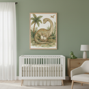 Modern nursery with a white crib against a sage green wall. A light wood framed illustration of a long-necked dinosaur looking at a nest of eggs and a hatching baby dinosaur hangs above the crib. A wooden dresser with a lamp and toy dinosaur is to the right, and a cream armchair is to the far right.