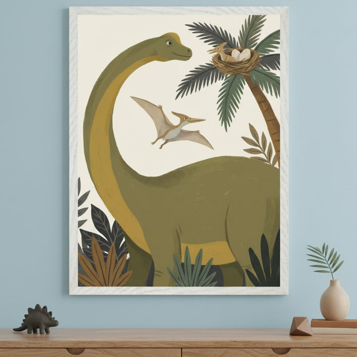 Framed illustration featuring a friendly green long-necked dinosaur, a flying pterodactyl, a palm tree with a nest of eggs, and jungle plants. It hangs centered above a light wooden dresser in a modern child's room with a light blue wall.