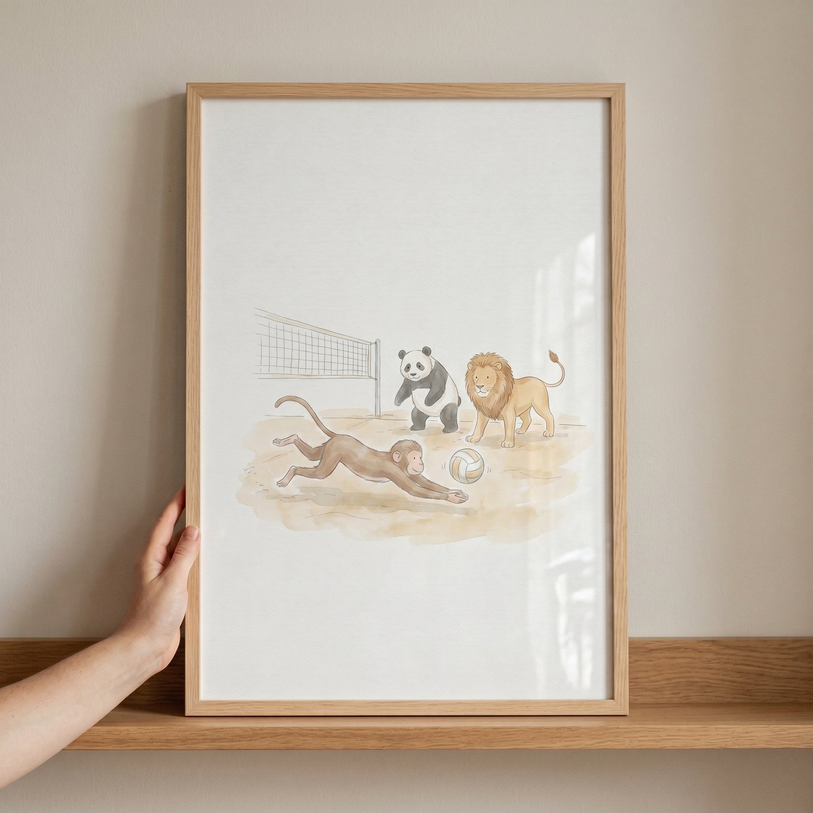 Hand holding diving volleyball animals wall art in a light wood frame with a monkey, panda, and lion playing on a beach.