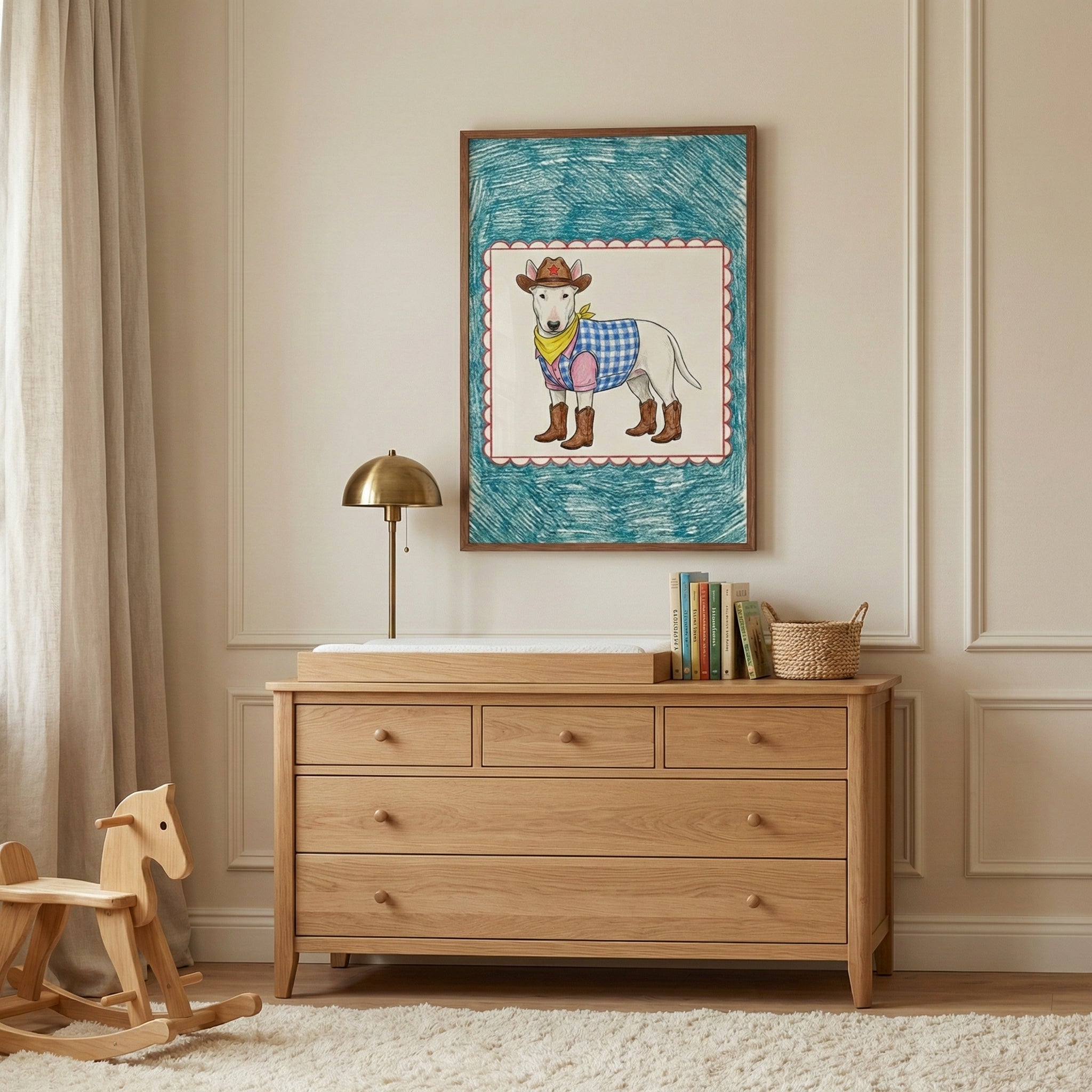 A framed illustration of a bull terrier dressed in cowboy boots and a blue checkered vest hangs above a wooden nursery dresser. The warm-toned room includes a brass lamp, a wooden rocking horse, and a cream-colored shag rug.