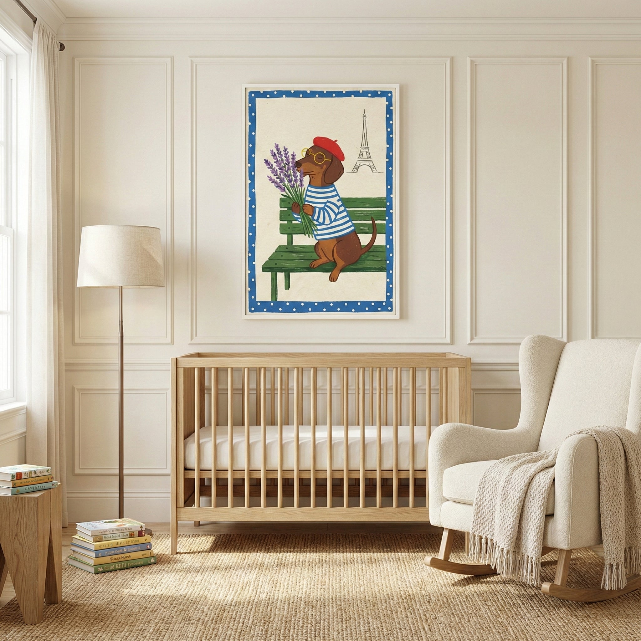 A neutral-toned nursery features a light wood crib centered against a paneled wall. Above the crib hangs a framed illustration of a small brown dog wearing a red beret and a blue-and-white striped shirt, sitting on a green park bench and holding a bunch of lavender. The illustration includes a simple line drawing of a famous landmark tower in the background and is framed by a blue border with white polka dots. To the right of the crib is a cream-colored rocking chair with a knit throw blanket draped over it