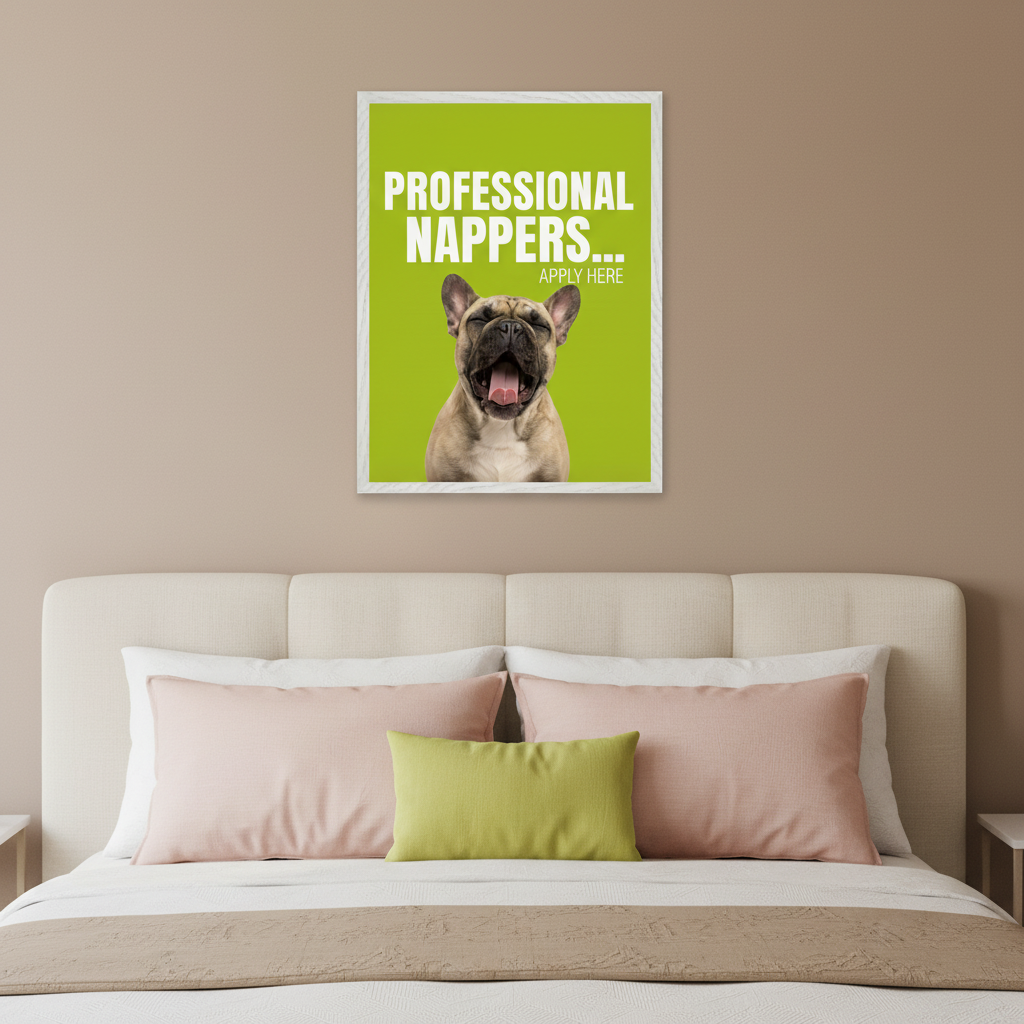Modern bedroom with a beige upholstered bed and colorful pillows. A white framed poster hangs centered above the bed. The artwork shows a yawning French bulldog on a bright green background. White text reads "PROFESSIONAL NAPPERS... APPLY HERE".