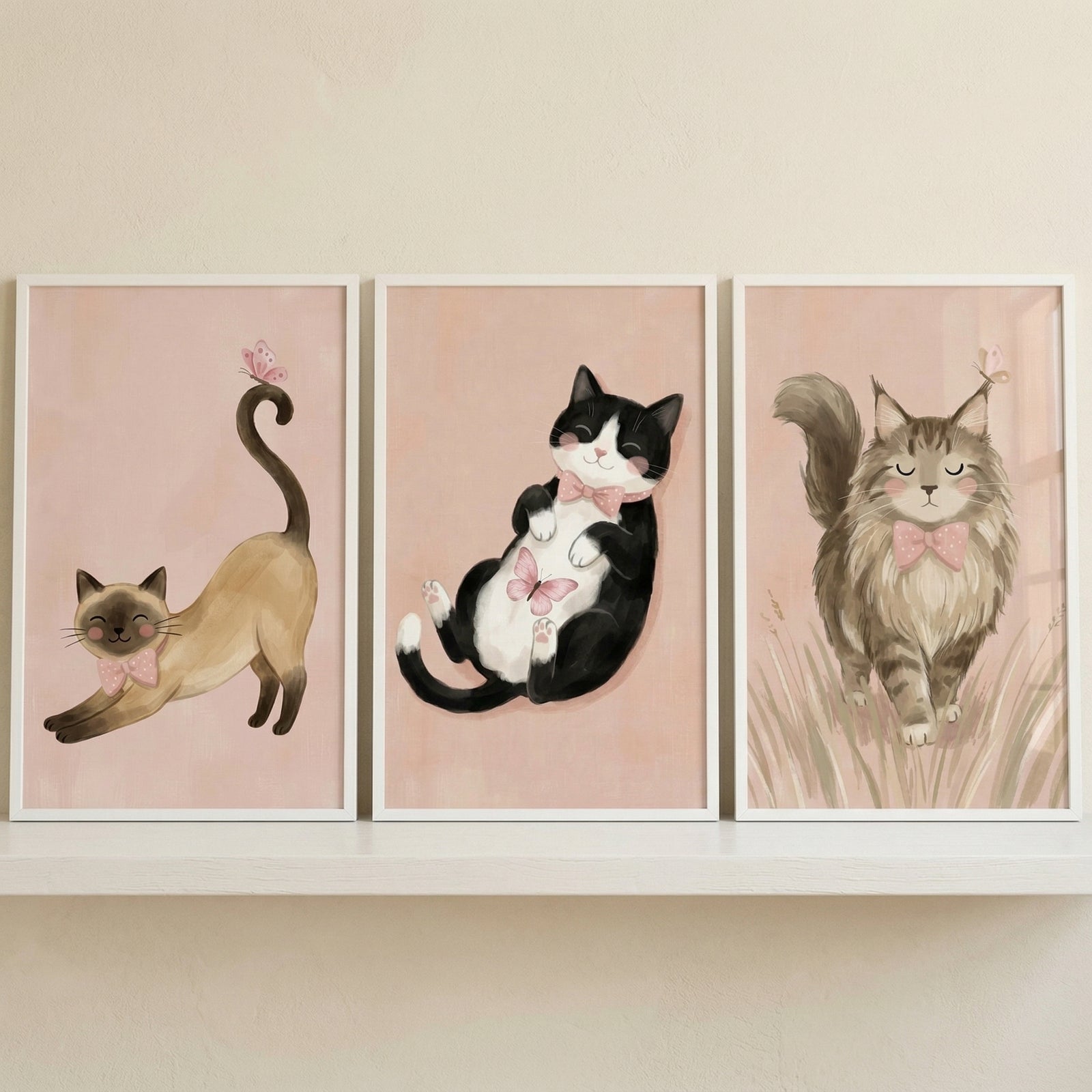 A set of three framed illustrations featuring different cats is displayed side-by-side on a white floating shelf. Each artwork is set against a soft, pale pink background.

In the first illustration on the left, a slender tan cat with dark markings on its face and paws is shown stretching, its tail curled high with a tiny pink butterfly on the tip. It wears a small pink bow tie.
