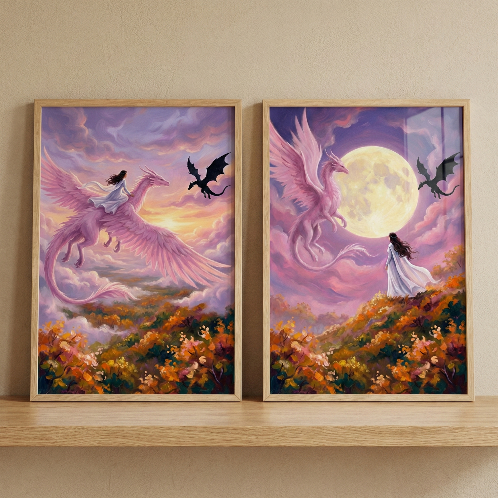 Two framed fantasy illustrations rest on a wooden shelf. The left piece shows a figure in a white dress riding a large pink feathered dragon through a purple sunset sky, with a small black dragon silhouette nearby. The right piece depicts the same figure standing on a flowered hillside, gazing up at a massive full moon. The pink dragon flies gracefully across the moon's face, and the black dragon follows. Both works feature a soft, ethereal style with warm autumn-colored landscapes.