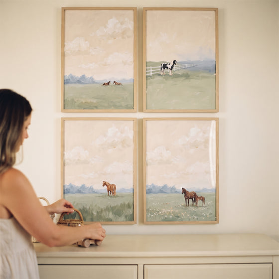 A woman stands by a dresser below a dreamy hazy field horses wall art set of 4 depicting horses in soft meadows.