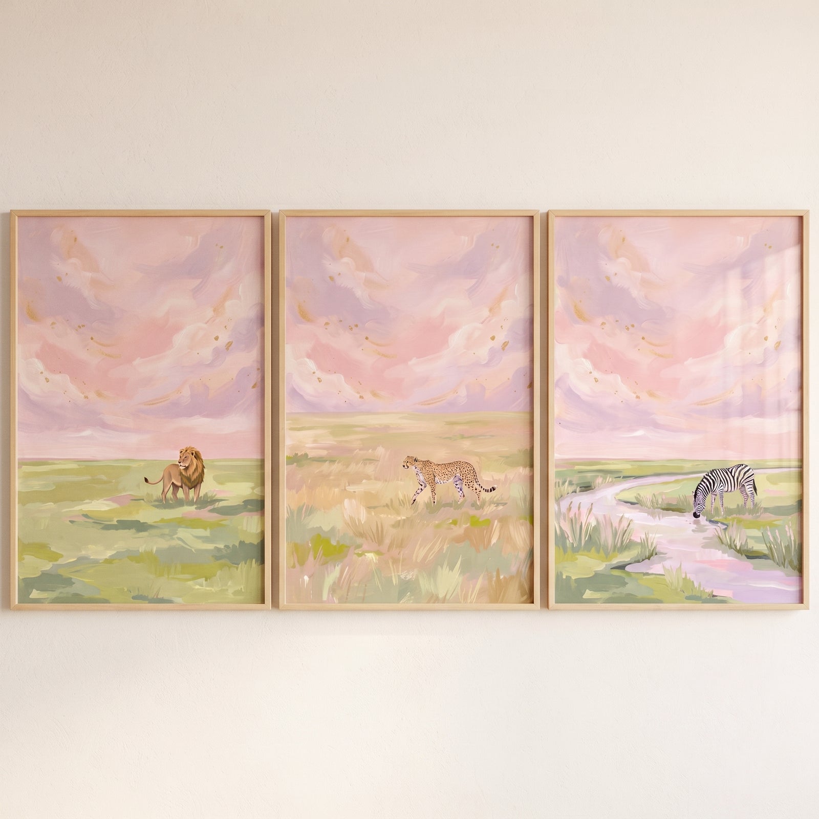 Dreamy pink safari animals wall art set of 3 with a lion, cheetah, and zebra drinking from a stream under a pastel sky.