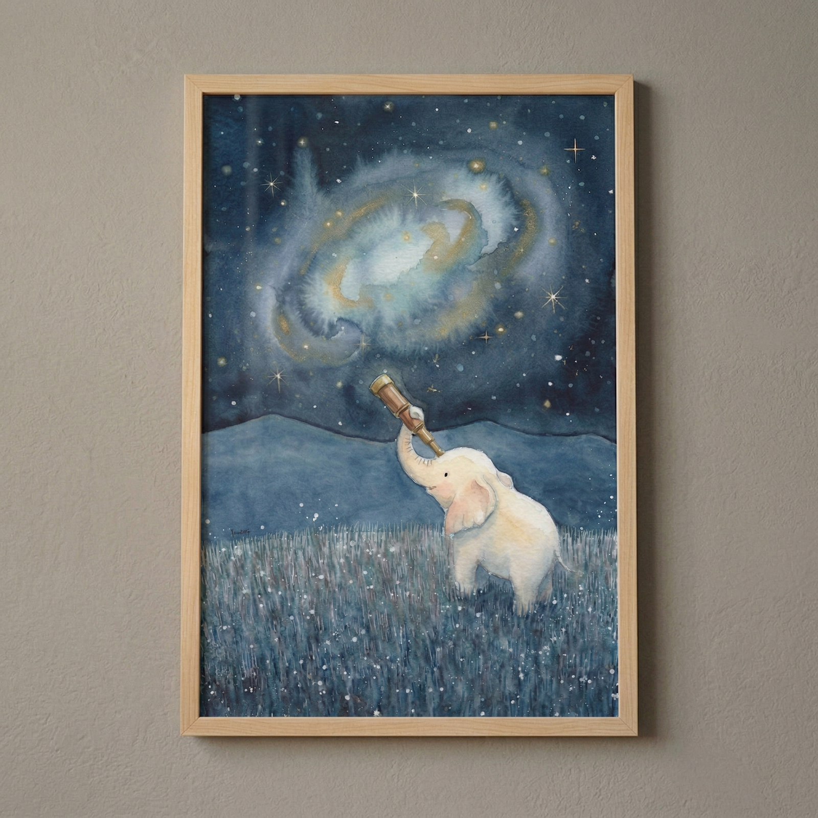 A framed watercolor-style illustration shows a small, white cartoon elephant in a field of dark blue grass with tiny white dots. The elephant holds a telescope with its trunk, looking up at a vast night sky. Above it, a large, glowing galaxy swirls in soft blue and gold tones, surrounded by many twinkling stars. Silhouetted mountains are visible in the distance. The artwork is held in a light wooden frame against a neutral-colored wall.