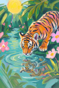 A tiger crouches at the edge of a stream drinking water as ripples form around its reflection. Pink flowers and leafy plants surround the bright jungle setting. The tiger’s focused posture captures a quiet moment.
