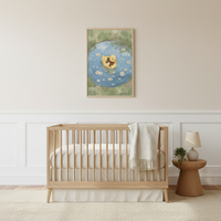 A minimalist nursery features a light wood crib centered against a cream wall with white wainscoting. Above the crib hangs a framed illustration of a small yellow duckling wearing a brown bow, swimming in a blue pond filled with white flowers. A chunky, off-white knit blanket is draped over the right side of the crib. To the right, a round wooden side table holds a simple lamp and a small potted plant. The room is completed by a light-colored, textured area rug on the floor.