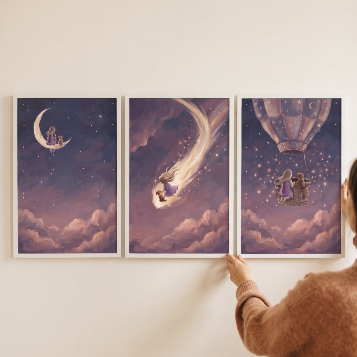 A person hangs a dusky violet girl dog wall art set of 3 with a girl and pet on a moon, a shooting star, and in a balloon.