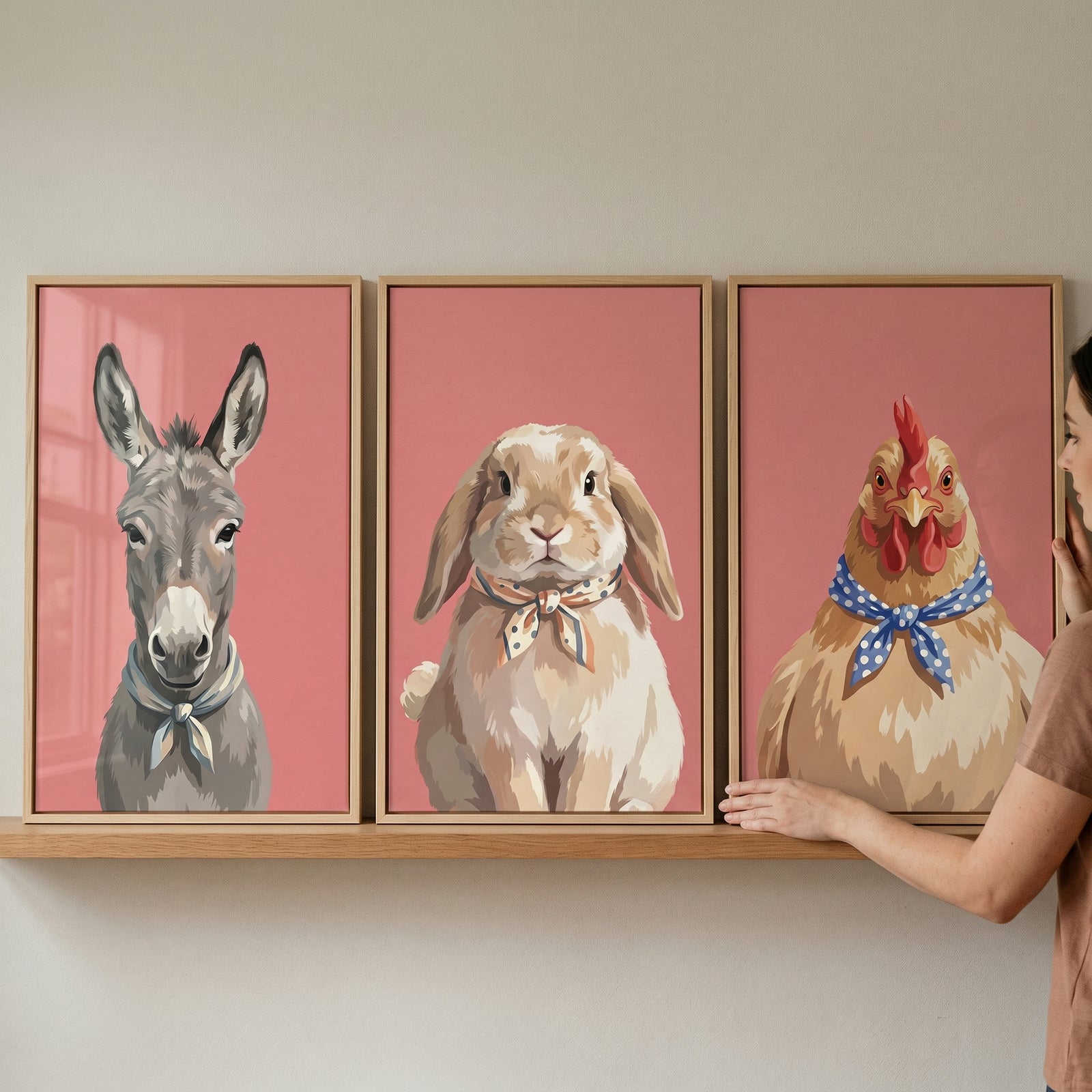 Hand adjusts a dusty rose farm animal wall art set of 3 featuring a donkey, rabbit, and chicken on a shelf.
