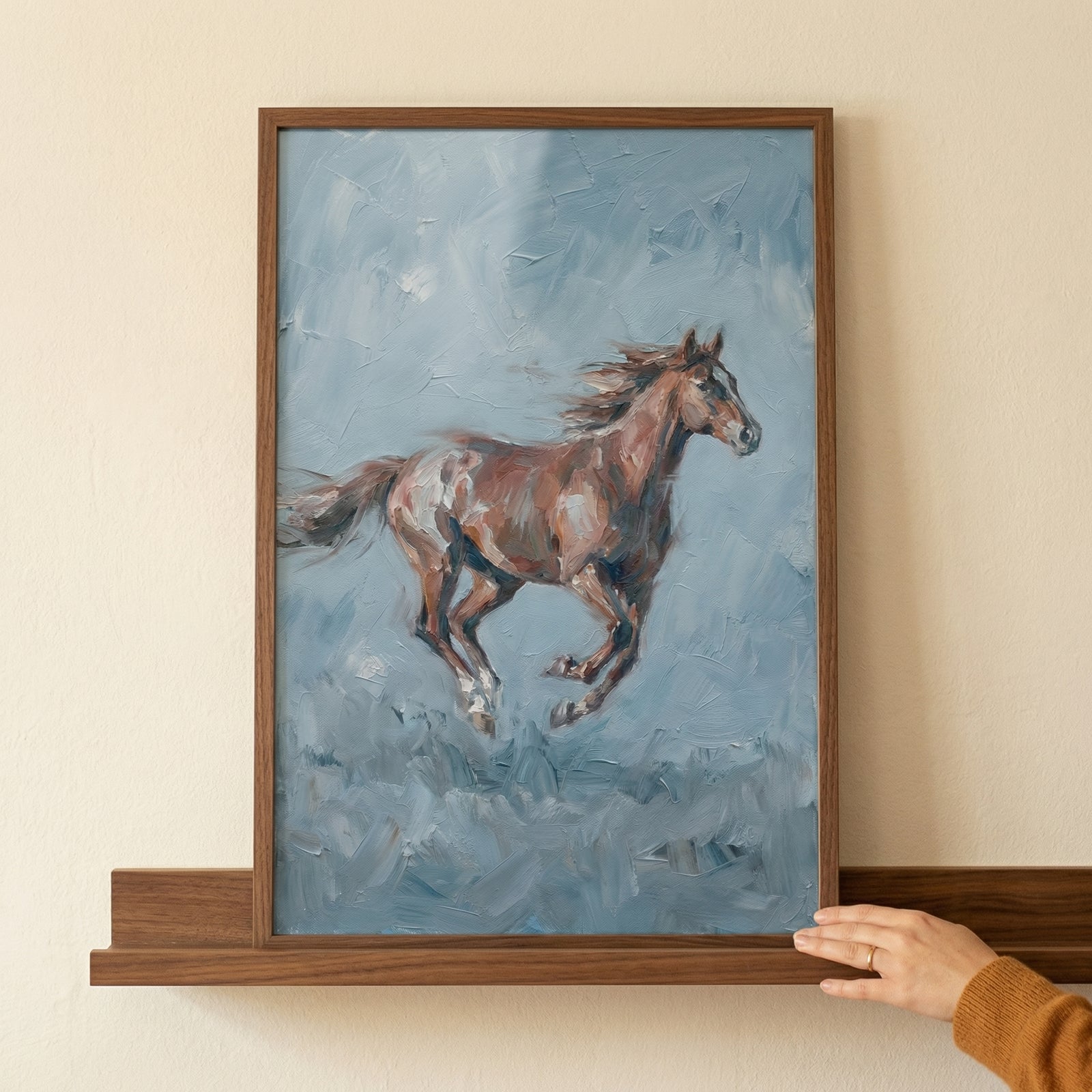 A vertical framed artwork depicts a reddish-brown horse in full gallop against a textured, swirling background of muted blue and gray tones. The horse is captured mid-stride, its mane and tail flowing to indicate rapid movement. 