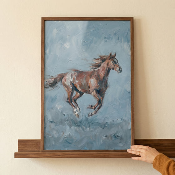 A vertical framed artwork depicts a reddish-brown horse in full gallop against a textured, swirling background of muted blue and gray tones. The horse is captured mid-stride, its mane and tail flowing to indicate rapid movement. 