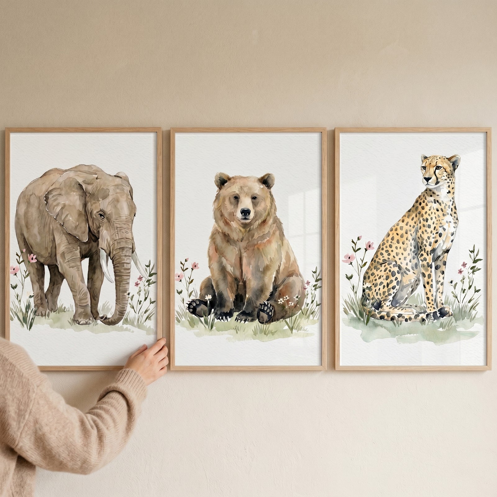 Hand touching an earthy botanical wildlife animal wall art set of 3 with an elephant, bear, and cheetah in wood frames.