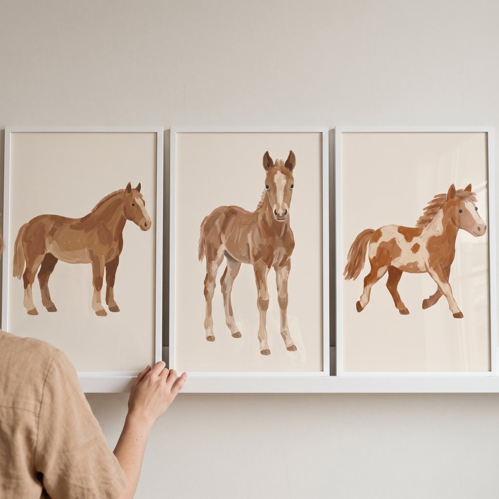 Hand touching an earthy brown chestnut horse wall art set of 3 featuring minimalist horse and foal illustrations.