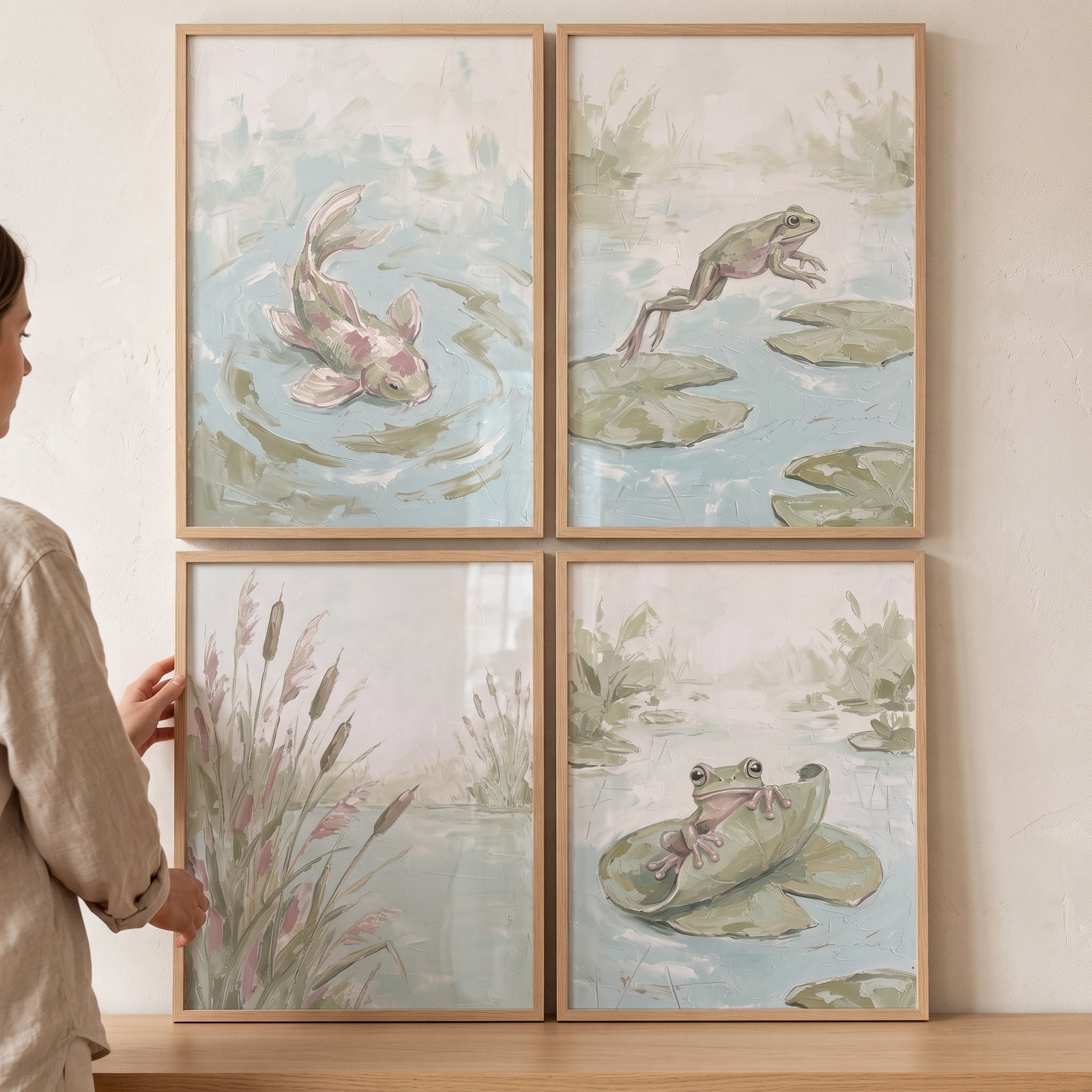 A person holds an earthy green pond wall art set of 4 featuring frogs, a fish, and reeds in light wood frames.
