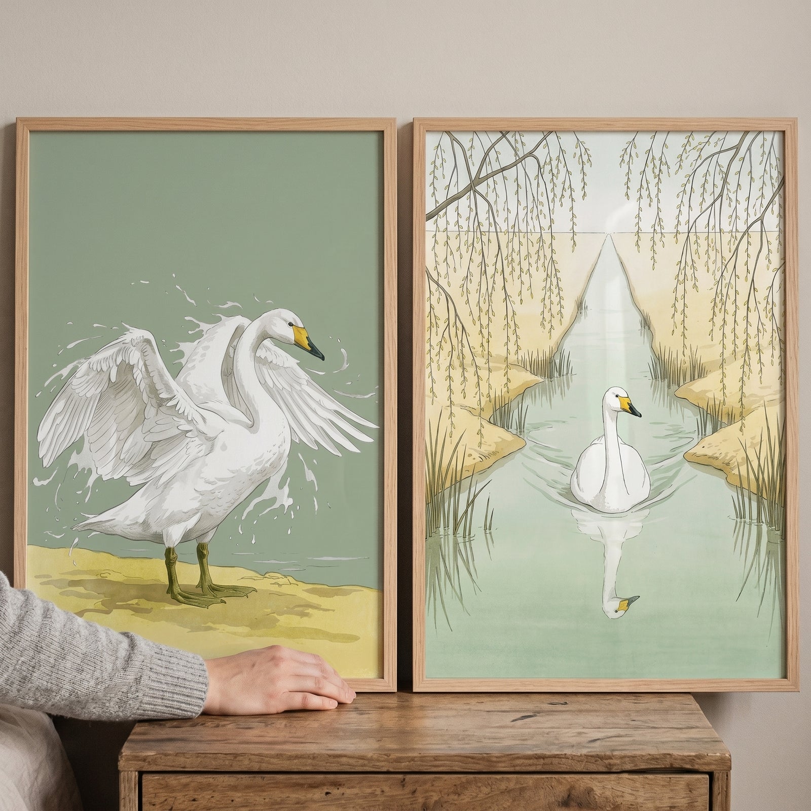 Earthy muted green swan wall art set of 2 shows one swan with open wings on a shore and another swimming under willows.